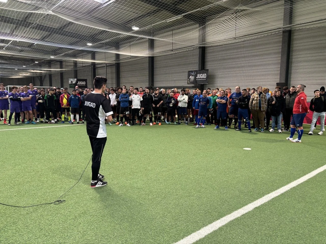 Julian spricht bei einem JUGAD-Turnier zu den Teilnehmenden auf einem Hallenfußballplatz.